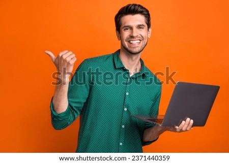 Photo of candid young positive guy brunet hair directing finger mockup all options his service laptop isolated on orange color background