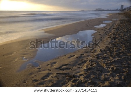 The sun is going to rise on the horizon, filling the entire Mediterranean beach with a warm light, where its puddles, coming from the waves that reach the seashore, the clouds are reflected