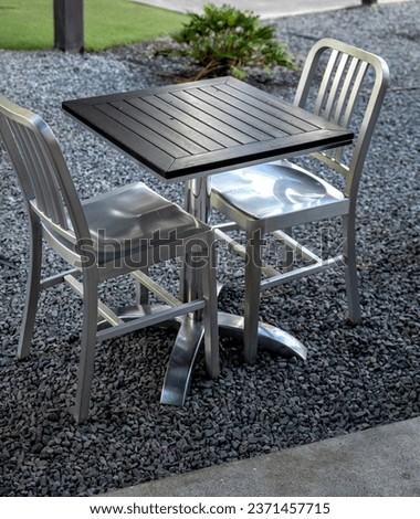 Silver Metal Chairs with a Black Topped Table on Gray Gravel.