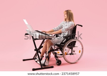 Young woman in wheelchair playing synthesizer on pink background Royalty-Free Stock Photo #2371458957