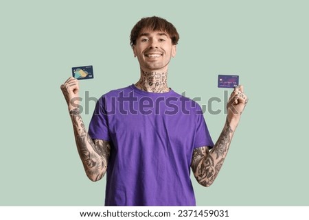 Tattooed young man with credit cards on green background
