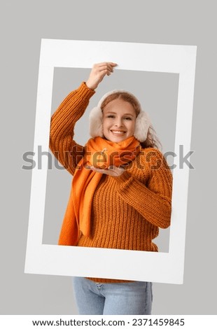 Young woman with pumpkin and frame on light background