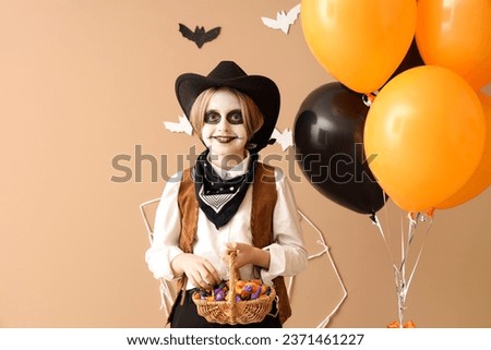 Little boy dressed for Halloween with candies and balloons near beige wall