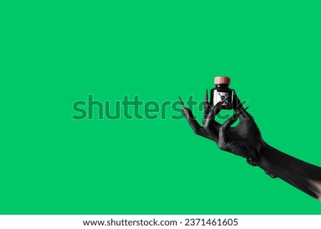 Black hand of witch holding bottle with poison on green background. Halloween celebration