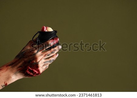Zombie hand holding cauldron with candies on green background. Halloween celebration