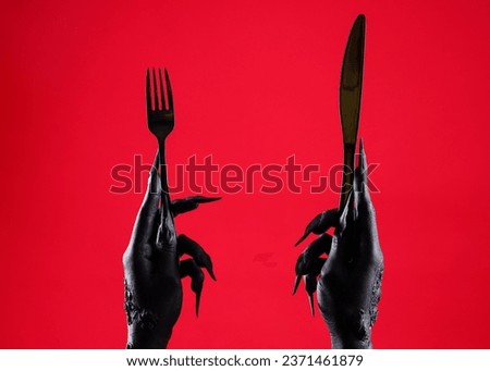 Black hands of witch with fork and knife on red background. Halloween celebration Royalty-Free Stock Photo #2371461879