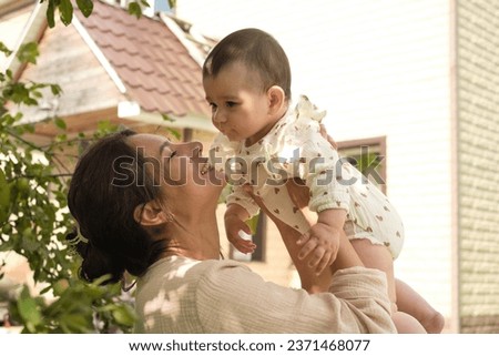 Nestled in the green sanctuary of her backyard, a young mom shares a magical moment with her baby, celebrating life's simple pleasures. How Green Spaces Positively Impact Mental Health Royalty-Free Stock Photo #2371468077