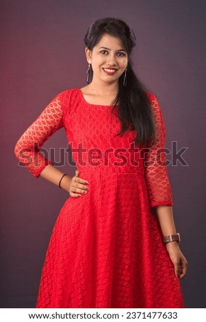Portrait of a beautiful, smiling, young Indian girl wearing a red dress posing on a dark background 