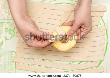 A woman's hands wrap an apple ring with a strip of puff pastry for baking in the oven. Home cooking. Royalty-Free Stock Photo #2371480875