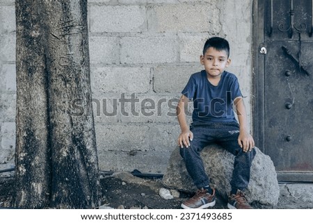latino boy sitting on a rock outside his home