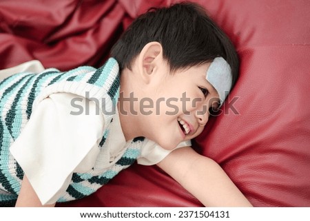 Asian boy Lying sick with a fever reducing patch on her forehead but still smiling. Royalty-Free Stock Photo #2371504131