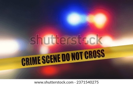"CRIME SCENE DO NOT CROSS" police tape in front of a blurred police car at night with its lights on.