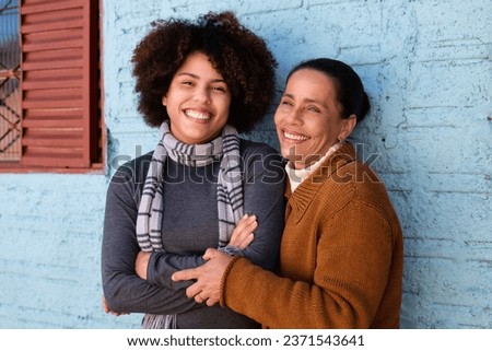 Happy cheerful black adult daughter and mother with broad smile embracing each other outside humble home Togetherness, family, support concept. Royalty-Free Stock Photo #2371543641