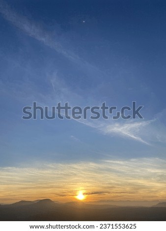This picture is a picture of the sun rising in the morning, the orange light contrasting with the bright blue sky, ready to start a new day.