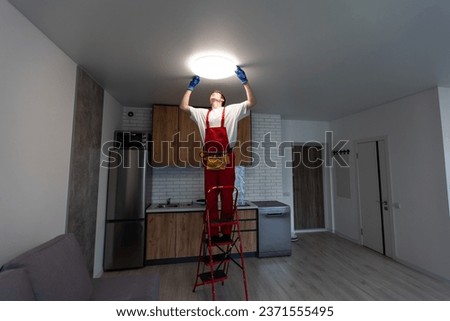 Electrician at work. Service for the repair of electrical wiring and replacement of ceiling lamps. A builder is installing a loft-style wooden ceiling. Rent-a-gent helps with the housework