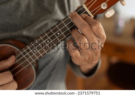 Detail of unrecognizable man's hand playing a chord on the ukulele Royalty-Free Stock Photo #2371579751