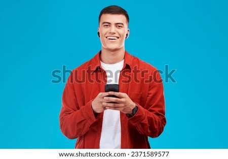 Man, earphones and smile with phone for communication in portrait, studio and happy by blue background. Asian male model, text and chat on smartphone while streaming music, song and audio or podcast