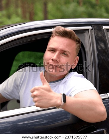 Young happy man satisfied driver show thumb up from opened window of his car and smile