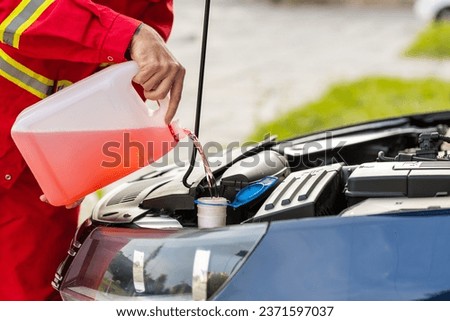 Close-up service worker man driver pouring non freezing windshield cleaning glass washer fluid into hood car tank from canister bottle. Summer or winter fluid windscreen liquid glass window cleaner