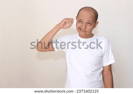 Expression of a bald Asian Indonesian wearing a white t-shirt against a white wall background