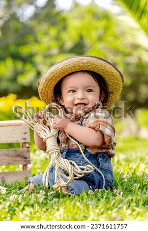 Happy baby smiling, dressed as a cowboy or farmer, sitting on th