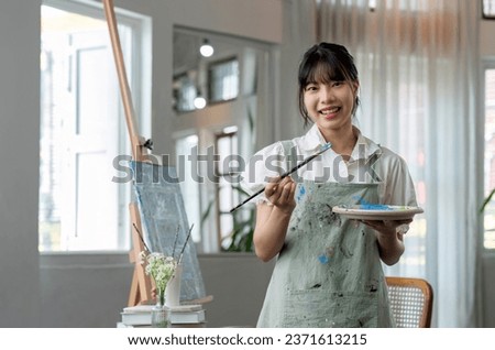 Portrait of a young female artist working on an abstract acrylic canvas painting in an art painting studio.