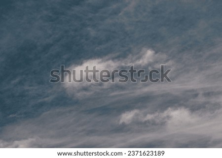 tuft of white cloud floating under a sky covered by a thin curtain of clouds, under a blue sky.