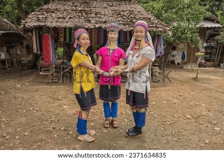 three long-necked Karen women with brass neck rings wearing traditional vibrant Karen style dress showing Karen dance in their rustic village at Pai in Mae Hong Son, Thailand