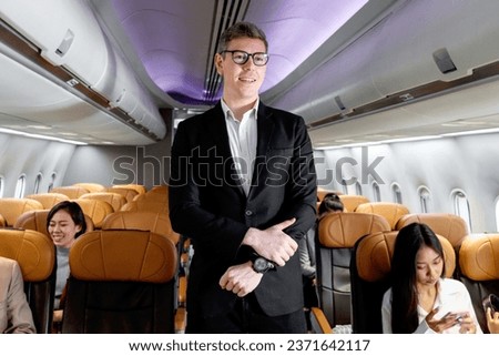 Portrait of happy smiling businessman in black suit, standing on aisle inside airplane, male passenger traveling on business trip by aircraft, businesspeople traveling with airline transportation. Royalty-Free Stock Photo #2371642117