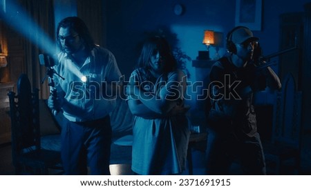 Medium-full photo capturing two ghost hunters and a victim going around the room in search for the cause of a paranormal activity, using EMF detector and filming it.