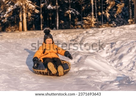 Active toddler boy in a yellow jacket sliding down the hill on snow tube.Winter fun,active lifestyle concept. Royalty-Free Stock Photo #2371693643