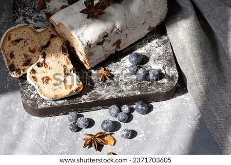 Traditional German Christstollen, winter holiday bakery. Bread or cake with raisins, blueberry and sugar powder. Stollen sliced on pieces, on wooden board.