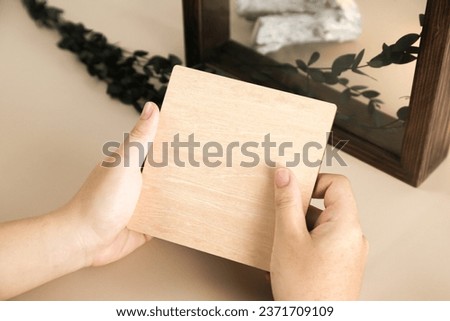 Young hands hold and write on wood board card beige background. Stock photo and blank product