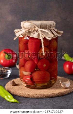 Pickled cherry tomatoes with sweet pepper and garlic in glass jar on brown table, Close up Royalty-Free Stock Photo #2371710227