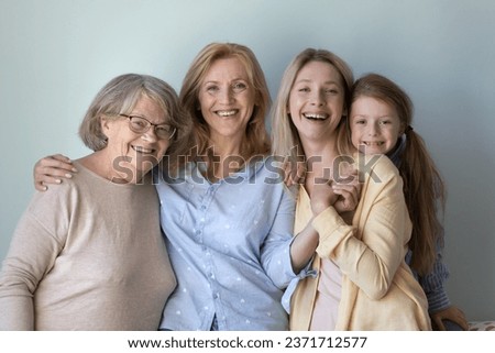 Happy kid, young mother, mature grandmother, senior great grandma portrait. Girl and women of four female generations standing at grey background, hugging with love, smiling, laughing