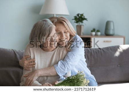 Happy loving mature daughter woman hugging old 80s mom with warmth, affection, devotion, visiting elderly mother, congratulating on birthday, 8 march day, enjoying family holiday