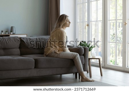 Thoughtful pretty young woman sitting on sofa indoors, looking away, thinking over bad concerning news, problem, troubles, feeling worried, lonely, making difficult decision Royalty-Free Stock Photo #2371712669