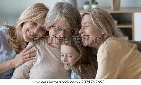 Happy cheerful girls and women of different family generations hugging great grandma with love, care, tenderness, gratitude, resting on sofa, smiling, celebrating birthday, mothers day