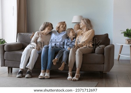 Four generations of happy joyful girls and women sitting on comfortable sofa in home, talking, chatting laughing, enjoying family leisure. Great grandmother, grandma, mom, daughter kid portrait