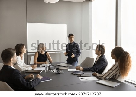 Confident young Indian manager presenting project report to diverse team, offering ideas, marketing strategy. Multiethnic colleagues with mature leader discussing cooperation Royalty-Free Stock Photo #2371712737