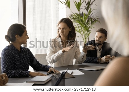 Happy engaged young employee woman offering creative marketing strategy, project plan, creative ideas for startup on brainstorming meeting, talking to multiethnic coworkers at table Royalty-Free Stock Photo #2371712913