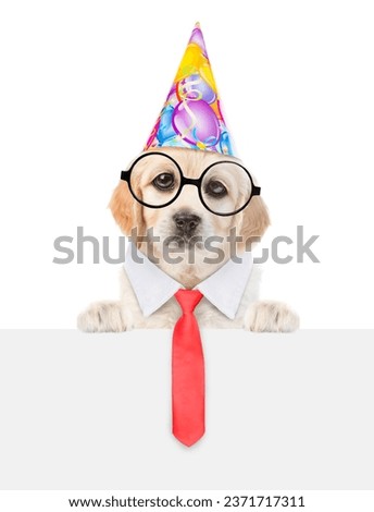 Golden retriever puppy wearing party cap, eyeglasses and necktie looks above empty white banner. isolated on white background