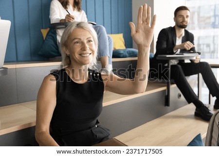 Positive senior learning employee woman raising hand on lecture, asking question to teacher, presenter, lecturer. Professional educating seminar audience listening to seminar, presentation Royalty-Free Stock Photo #2371717505