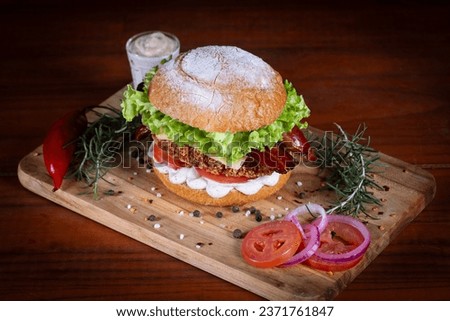 Chicken burger with bacon, lettuce, tomato, cheddar cheese and onion served on cutting board on a black wooden table. Craft chicken burger, hand made.
