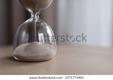 Sand passes through the bulbs of an hourglass, measuring the passage time in a countdown to the deadline, on a dark background with copy space. Royalty-Free Stock Photo #2371773401