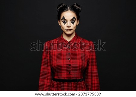 Young serious cool woman with Halloween makeup face art mask wearing clown costume red dress looking camera isolated on plain solid black wall background studio portrait. Scary holiday party concept