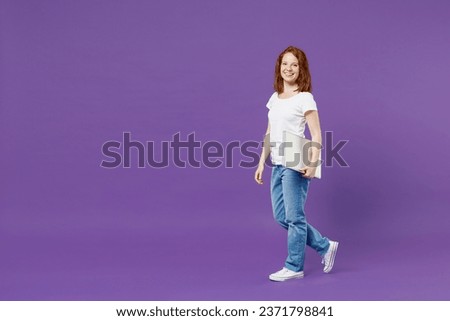 Full length young happy satisfied redhead IT woman wear white basic casual t-shirt holding using laptop pc computer chat online look camera isolated on dark violet color background studio portrait.