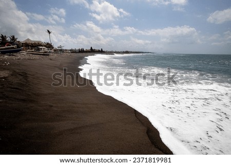 Black sand beach in Bali, natural with temples, boats (jukung) and waves at sunrise. Tropical environment in Indonesia in the morning