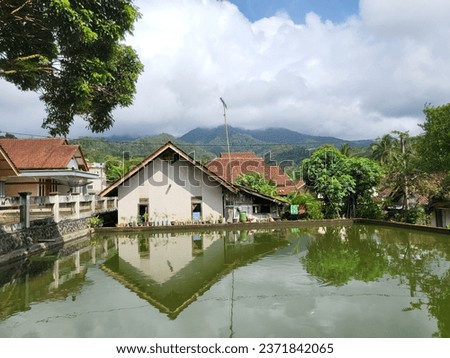 A fish pond in the yard of a rural house with a view of the sawal mountain in the background.
