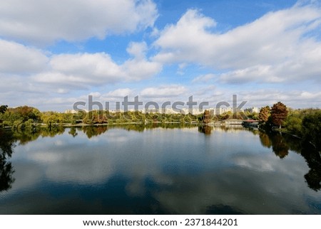 Landscape with many large green and yellow old trees near the lake in a sunny autumn day in Tineretului Park in Bucharest, Romania Royalty-Free Stock Photo #2371844201